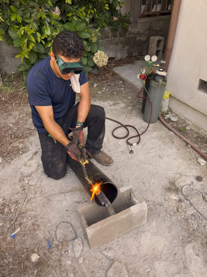Man using a torch to work on pipes outdoors.